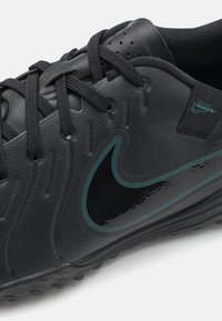 Black leather athletic shoe with textured surface, dark green Nike swoosh logo, and black laces. Features flexible rubber outsole with grip.