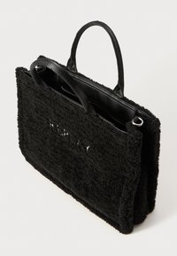 Zwarte tote bag met een gestructureerde, fuzzy buitenkant en gladde zwarte leren accenten, voorzien van dubbele stoffen handvatten en een ritssluiting.