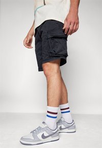 Black cargo shorts with side pockets, paired with white, red, and blue striped socks, and gray Nike sneakers with white accents.