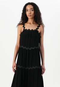 Μαύρο μέγιστο φόρεμα με σκαλπ παρόλες και οριζόντια σκαλπ περιθώρια. Φτιαγμένο από μαλακό ύφασμα με χαλαρή σιλουέτα και επίπεδα στρώματα.