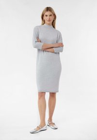 Graues gestricktes Kleid mit hohem Stehkragen, Dreiviertelärmeln und taillierter Silhouette, kombiniert mit silbernen flachen Schuhen.