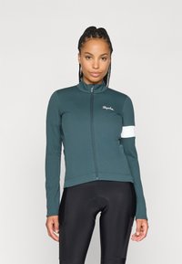 Chaqueta de ciclismo de manga larga en azul oscuro con cuello alto, cremallera frontal, cinta blanca en la manga y logo de Rapha, fabricada con material elástico y suave.