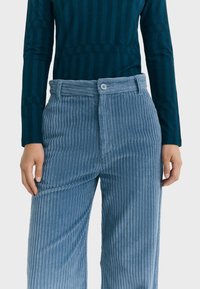 Lichtblauwe corduroy wide-leg broek met verticale ribbelstructuur. Taille met knoopsluiting, gestyled met een donkergroene gestreepte langemouwen top.