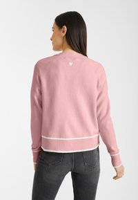 Roze gebreide trui met geribde onderrand en manchetten, voorzien van een witte streep en een klein hartje detail op de bovenrug.