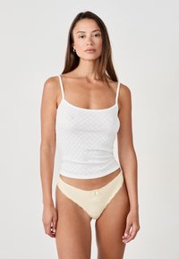 Top in cotone bianco con un motivo testurizzato, abbinato a un paio di mutande in satin giallo chiaro con pizzo e un piccolo dettaglio a fiocco.