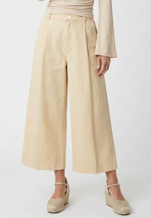 Beige weit geschnittene, gekürzte Hose getragen mit einem beigen Langarmtop und Keilabsatz-Espadrilles mit Knöchelriemen.