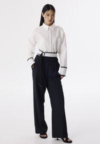 Chemise blanche à boutons avec une poche avant, assortie à un pantalon ample marine avec une ceinture noire et des sandales à talons noires.