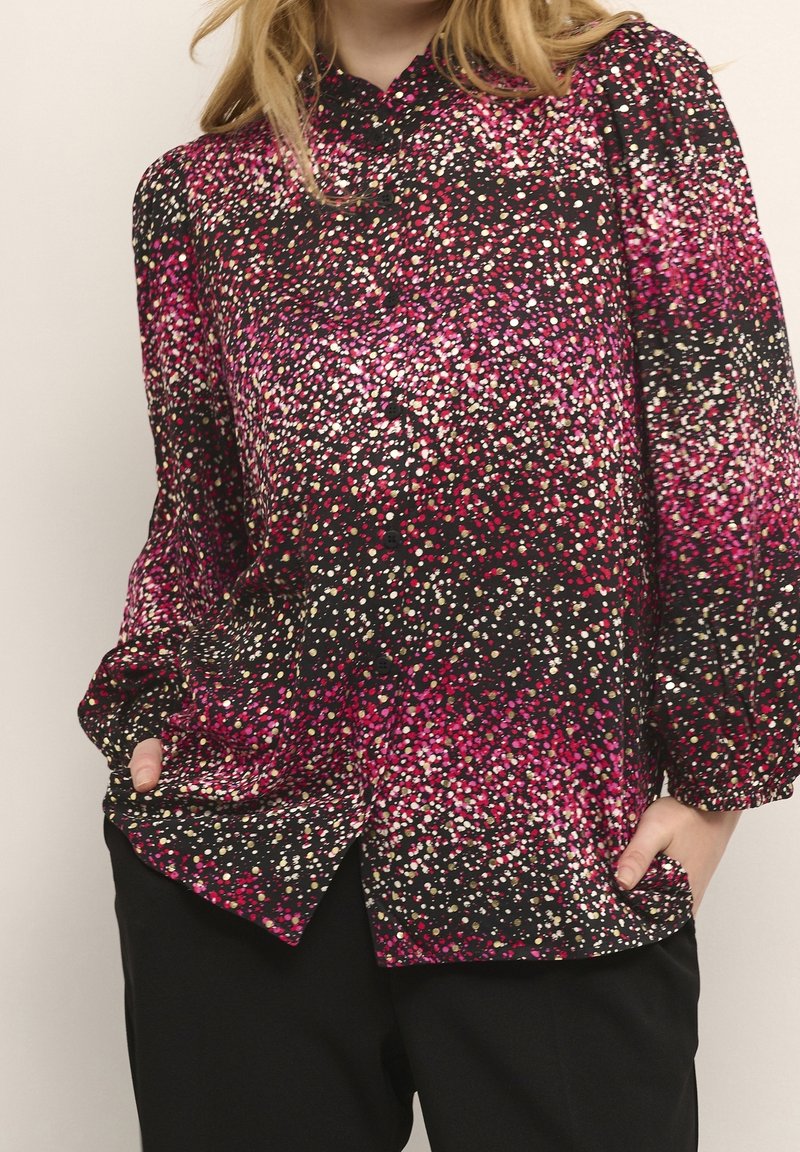 Svart blus med lång ärm och ett färgglatt, prickigt mönster i rosa, vitt och rött. Har knäppning framtill och en oversized passform.