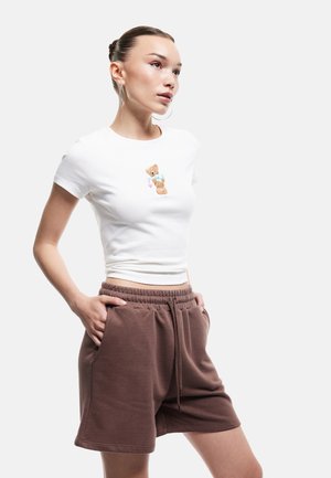 T-shirt en coton blanc avec un graphique de ours en peluche, associé à un short en polaire marron. Le short possède des poches latérales et une taille élastique.