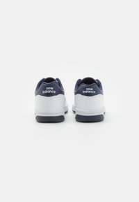 Hvide og marineblå atletik-sko med en glat syntetisk overdel og gummisål, udstyret med et fremtrædende "new balance" logo på hælen.