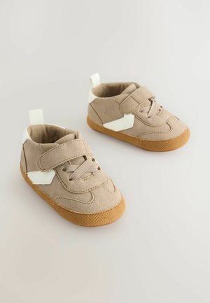 Zapatillas para niños pequeños de ante beige con detalles blancos y cierre de velcro, con suela de goma texturizada y diseño que brinda soporte al tobillo.