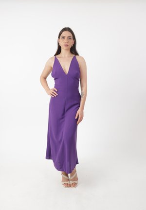 Robe sans manches violette avec un décolleté en V profond, tissu lisse, design ajusté et jupe fluide ; assortie à des talons de couleur claire.