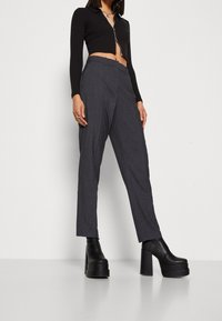 Svart cropped topp med dragkedja framtill, i kombination med mörkgrå skräddarsydda byxor. Modellen bär klumpiga svarta platåstövlar. Enkel och stilren design.