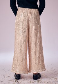 Pantaloni a gamba larga in rosa pallido con paillettes, caratterizzati da una superficie testurizzata con righe verticali di paillettes e una cintura elastica.