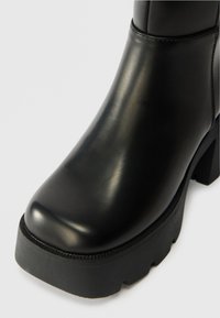 Melnas ādas potīšu zābakus ar noapaļotu pirkstu, biezu melnu zoli un teksturētu šuvi gar malu. Gluda, pulēta virsma.