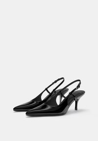Talons aiguille en cuir verni noir à brides arrière, avec des pointes en forme de doigts de pied, des sangles fines et un talon stiletto d'une hauteur intermédiaire. Comprend des découpes sur les côtés.