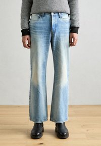 Lichtblauwe denim wijde jeans met vervaagde patches, vijf-pocketontwerp en een knoopsluiting, gecombineerd met zwarte leren enkellaarsjes.
