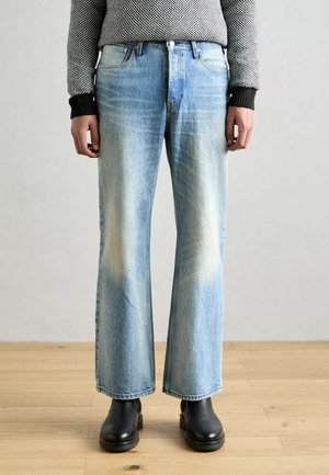 Lyseblå denim brede bukser med falmede lapper, fem-lommers design og knappelukking, kombinert med svarte lær ankelsko.
