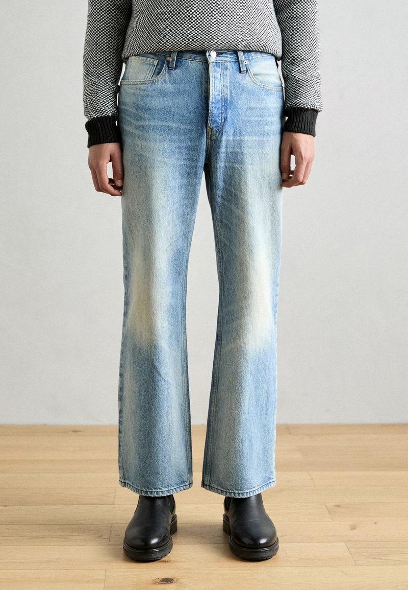 Lichtblauwe denim wijde jeans met vervaagde patches, vijf-pocketontwerp en een knoopsluiting, gecombineerd met zwarte leren enkellaarsjes.