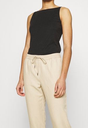 Top nero senza maniche in tessuto morbido, con scollatura quadrata. Abbinato a pantaloni beige con coulisse, dotati di tasche laterali e dal taglio morbido.