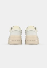 Weiße und beige Sneakers mit einer strukturierten Laufsohle, abgerundetem Design und Markenlogo an der Ferse. Obermaterial aus glattem Leder mit subtilen Farbakzenten.