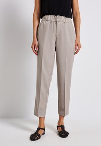 Beige tailored trousers with a high waistband, two front buttons, and a relaxed fit. Lightweight fabric with a smooth texture, paired with black sandals.