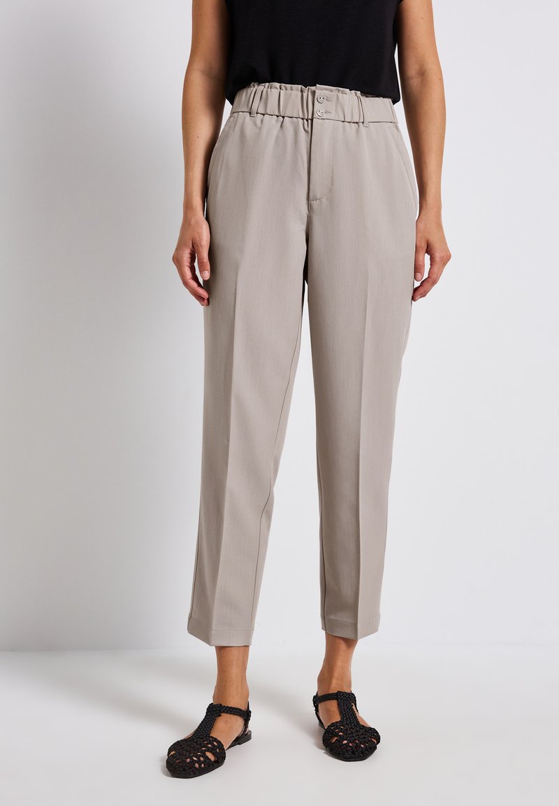 Beige tailored trousers with a high waistband, two front buttons, and a relaxed fit. Lightweight fabric with a smooth texture, paired with black sandals.