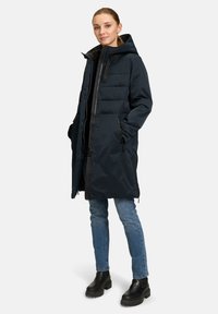 Marineblauwe pufferjas met een ritssluiting aan de voorkant, een capuchon en twee zijzakken, met een gestructureerde afwerking en verstelbare trekkoorden.