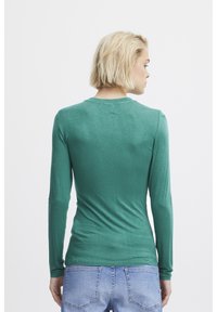 Grön långärmad skjorta med en åtsittande design och ribbad struktur, med en rund halsringning och slätt tyg, tillsammans med ljusblå jeans.