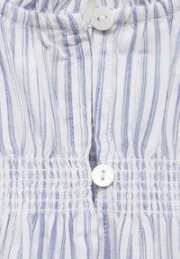 Tessuto bianco con strisce blu presenta un bottone centrale e una sezione elastica arricciata, evidenziando un design casual e testurizzato.
