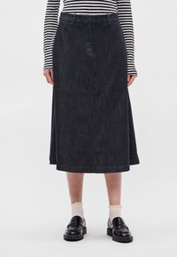 Μίντι φούστα από τζιν σε σκούρο wash με ίσια γραμμή, θηλιές για ζώνη και υποβλητή υφή. Συνδυασμένη με μαύρες μονοκές και κρεμ κάλτσες.