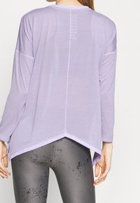Light lavender long-sleeve top with a rounded neck, drop shoulders, and a high-low hem. Made of soft, lightweight material.