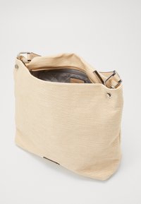 Beżowa torba na ramię z plecionki o teksturowanym wykończeniu, z górnym otwarciem i srebrnym metalowym zapięciem. Wnętrze ma kontrastową szaro-skalową podszewkę.