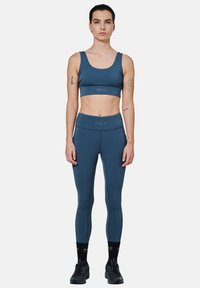 Blauwe set van sportbeha en legging met een gladde textuur. Bevat subtiele branding en een aangesloten ontwerp, gecombineerd met zwarte sneakers.