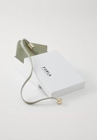 Portafoglio in pelle verde chiaro con dettagli in oro, presentato in una scatola bianca con il nome del marchio "Furla."