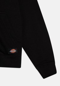 Manga de sweatshirt preta com punhos canelados, um bolso frontal e um emblema com logo colorido perto da bainha. Material em mistura de algodão.