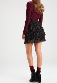 Falda corta negra de varios niveles con estampado de lunares, combinada con una blusa de manga larga burdeos y botas negras hasta el tobillo, mostrando texturas suaves.