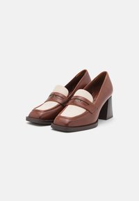 Mocasines de cuero marrón con un acento en crema, punta cuadrada y tacón grueso. Presenta una tira decorativa y detalles de costura. Textura suave.