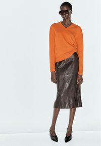 Orange knit v-neck sweater paired with a brown leather midi skirt and black pointed-toe heels. Model wears dark sunglasses.