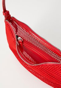 Rudá síťová kabelka s uzávěrem na zip, elegantní kožené detaily a vnitřní kapsa. Textura je otevřená a lehká.