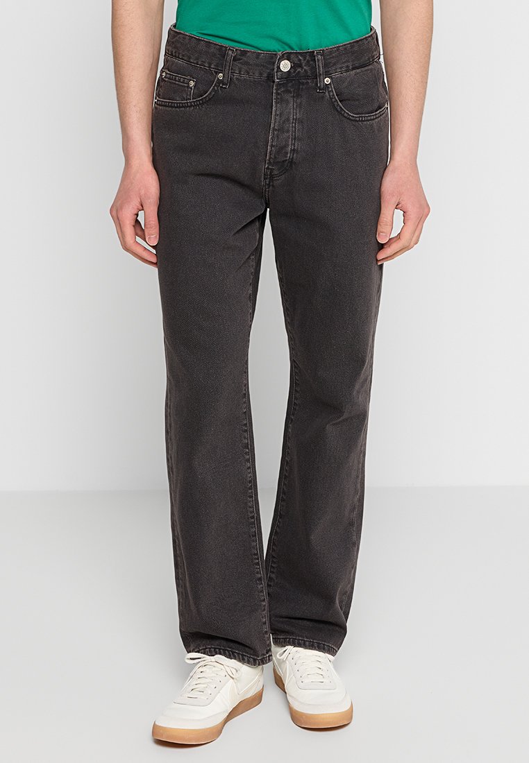 Jeans de mezclilla negra con un diseño de pierna recta, cinco bolsillos y detalles de costura sutiles, combinados con zapatillas deportivas blancas.