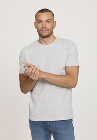 T-shirt en coton gris avec un col rond et des manches courtes. Le détail notable comprend une petite touche orange à l'ourlet.