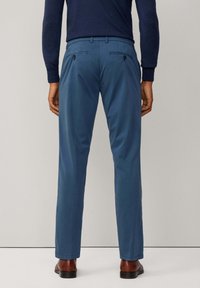 Pantaloni azzurri chiari con una texture liscia, passanti per cintura e due tasche posteriori, abbinati a scarpe marroni, visti da dietro.