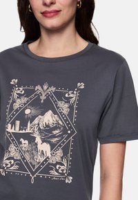 Anthrazitgraues T-Shirt mit einem cremefarbenen Grafikdesign, das Berge, eine Sonne und Pferde in einem Rautenmuster zeigt.