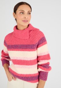 Maglione lavorato a maglia nei colori rosa, crema e viola a righe. Collo alto, texture a costine e polsini arrotolati. Design morbido e spesso per garantire calore.