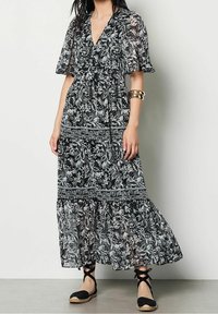 Svartvit blommig maxiklänning med V-hals och fladderärmar, med en lager-på-lager kjol och intrikata bladmönster.