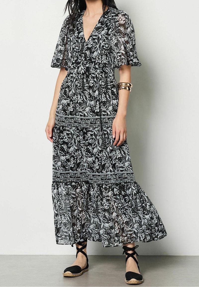Svartvit blommig maxiklänning med V-hals och fladderärmar, med en lager-på-lager kjol och intrikata bladmönster.