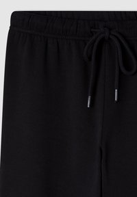 Czarne dresy z wysokością w pasie regulowaną sznurkiem, teksturowany materiał, elastyczne ściągacze na kostkach oraz metalowe akcenty na końcach sznurka.