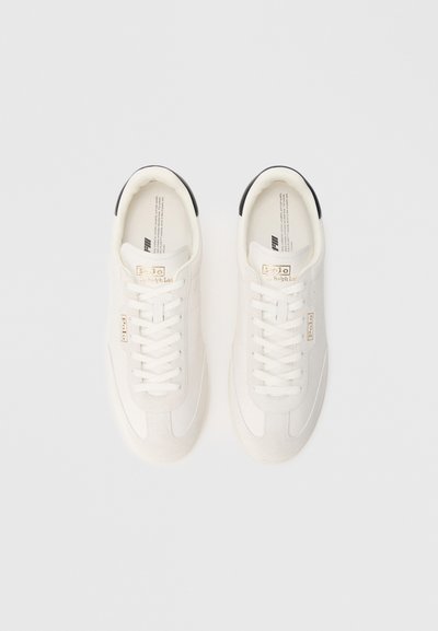 Balti sporta apavi ar gludu ādas virsmu, mežģīņu aizdari un melnu akcentu papēžā. Zelta logotipa detaļa pie mēles.