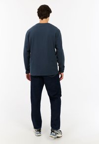 Donkerblauw shirt met lange mouwen, ontspannen pasvorm, met een ronde halslijn. Gekocht met donkere spijkerbroeken en gekleurde sneakers. Eenvoudig ontwerp, geen patronen.